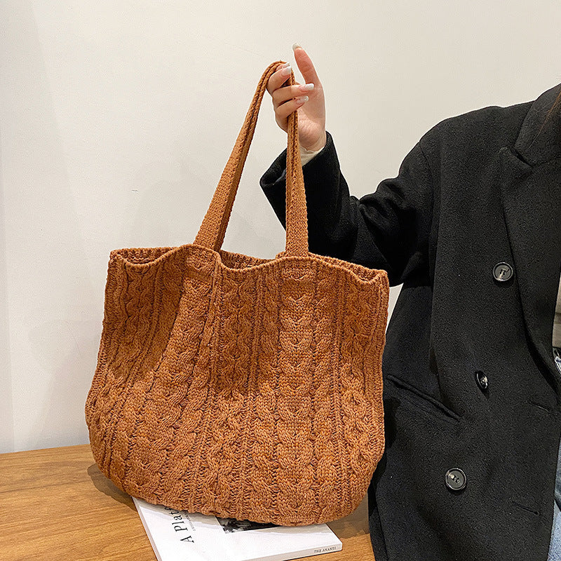Person holding a brown textured tote bag on a wooden surface with a neutral background