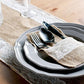 Set of gray plates with black cutlery on a lace and burlap runner on a wooden table.