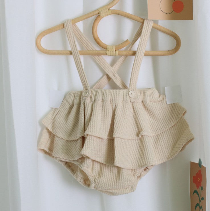 Beige ruffled baby outfit with straps on a hanger against a white background