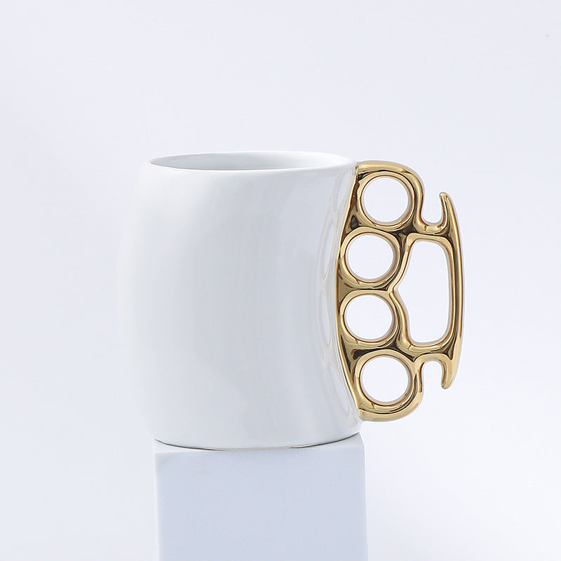White mug with a gold knuckle duster handle on a light gray background