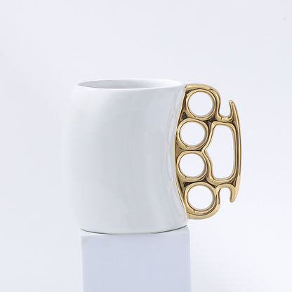 White mug with a gold knuckle duster handle on a light gray background