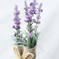 Vase of lavender flowers wrapped in burlap with a bow on a light background