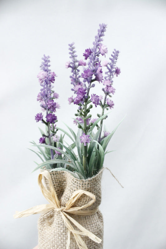 Vase of lavender flowers wrapped in burlap with a bow on a light background