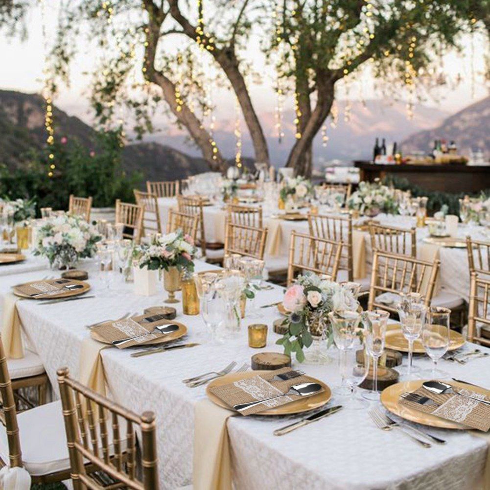 Elegant outdoor wedding reception with tables set for dinner, chairs, and floral arrangements under a tree.