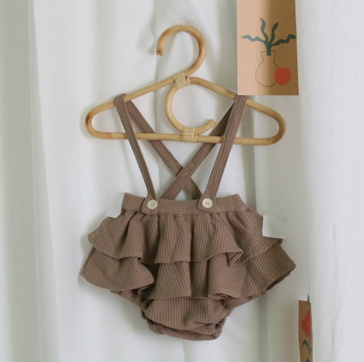Brown ruffled romper with suspenders on a wooden hanger against a white background