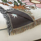 Decorative throw blanket with fringe on a floral-patterned surface