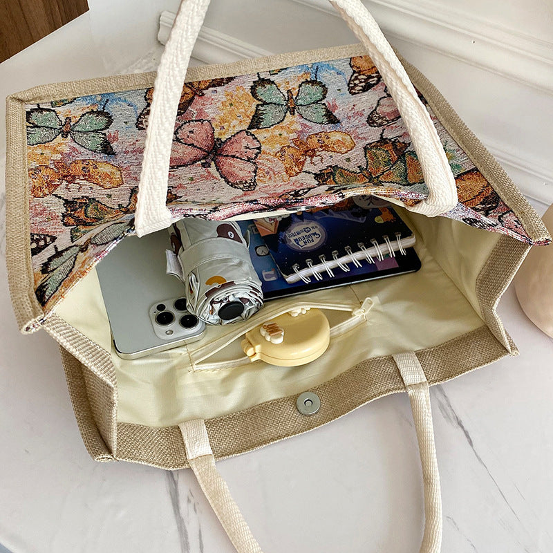 Tote bag with butterfly pattern interior, containing a phone, notebook, and other items.