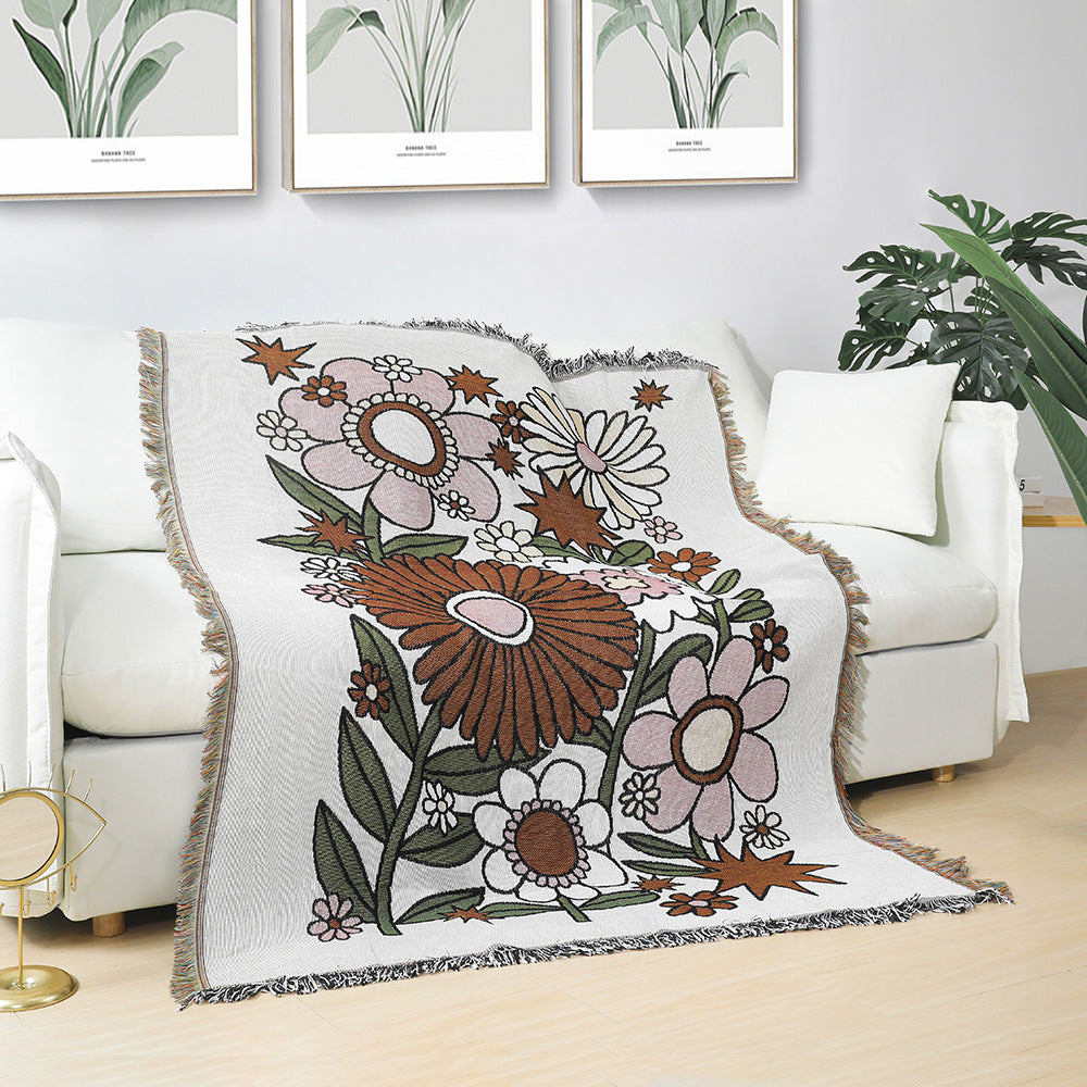 Floral patterned throw blanket on a white couch with plant-themed wall art in the background.