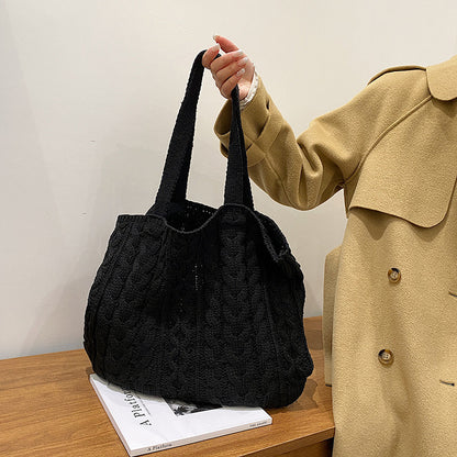 Person holding a black knitted bag next to a beige coat on a wooden surface.