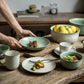 Dining table with ceramic dishes, cups, and food on a wooden surface.