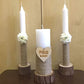 Three candles on wooden stands with floral decorations and a heart-shaped plaque on a beige background