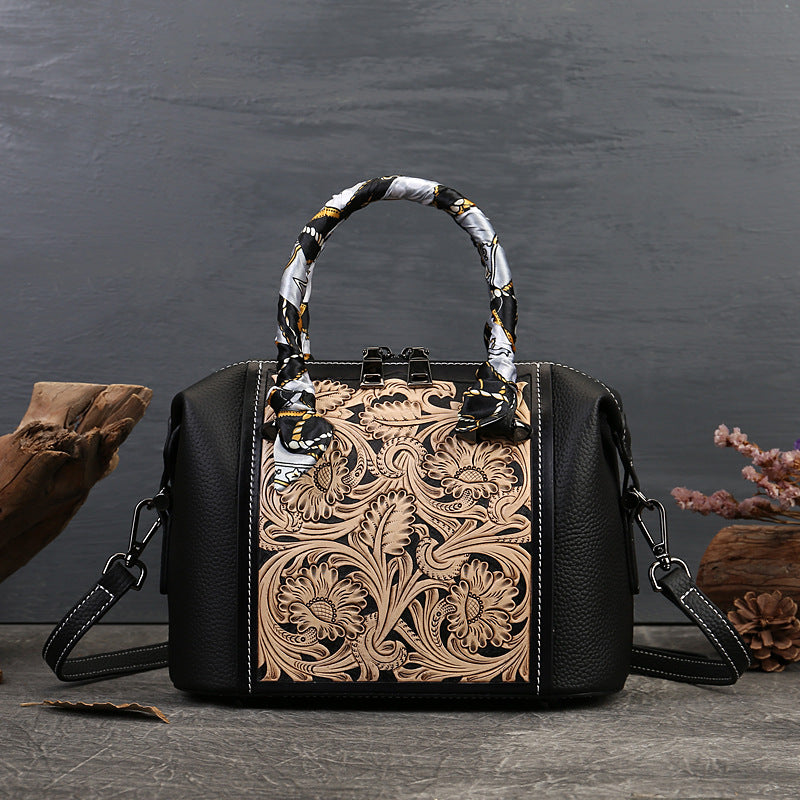 Black handbag with intricate floral tooled leather design on a dark background