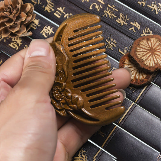 Hand holding a wooden comb with floral design on a textured surface