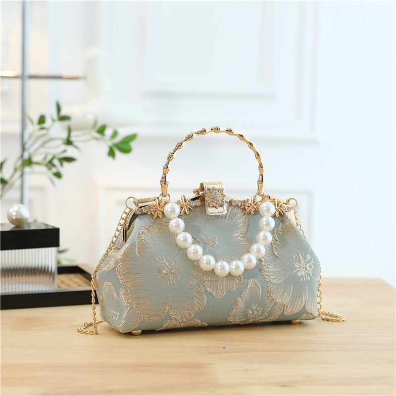 Decorative handbag with floral patterns and pearl chain on a wooden surface.
