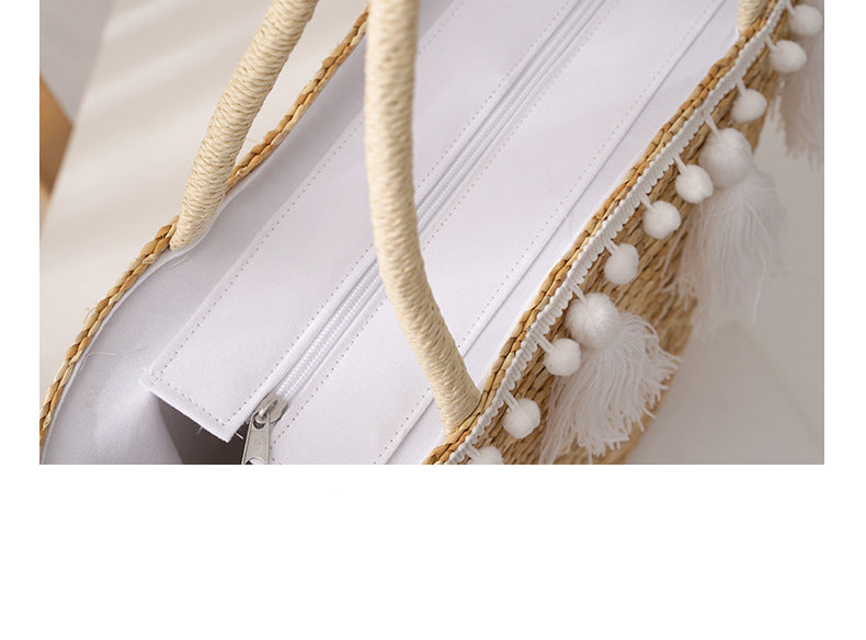 Close-up of a white bag with beige handles and tassels on a light background