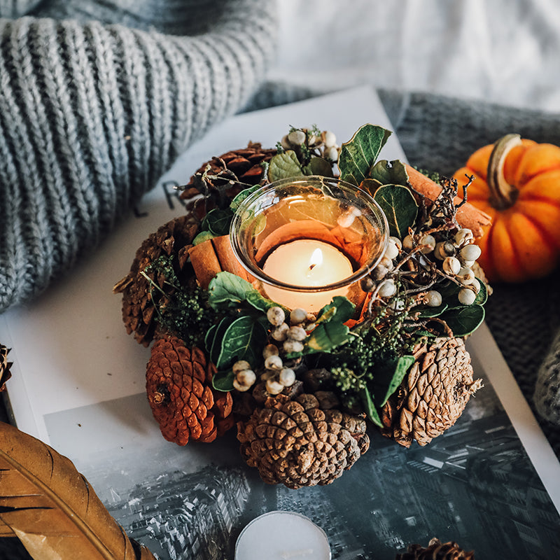 Decorative candle holder with pinecones, berries, and a small pumpkin on a marble surface.