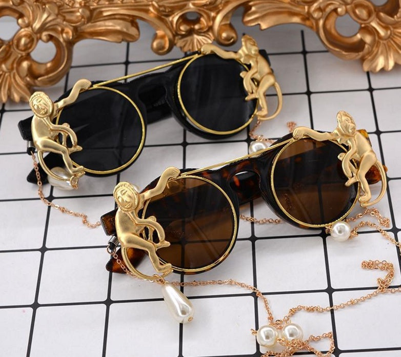 Sunglasses with gold monkey designs and pearl accents on a checkered surface.