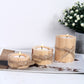 Three wooden candles with twine wrapping on a white surface with a plant in the background