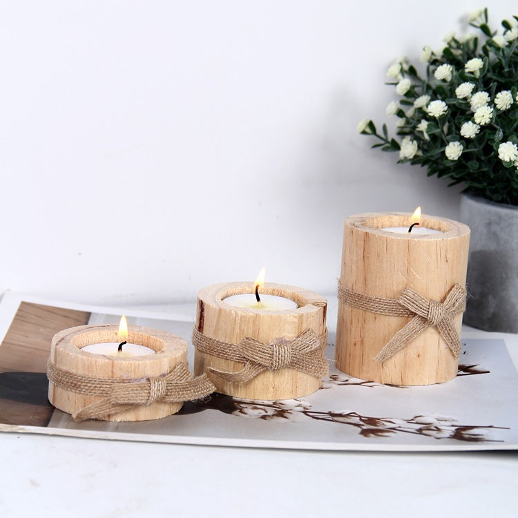 Three wooden candles with twine wrapping on a white surface with a plant in the background