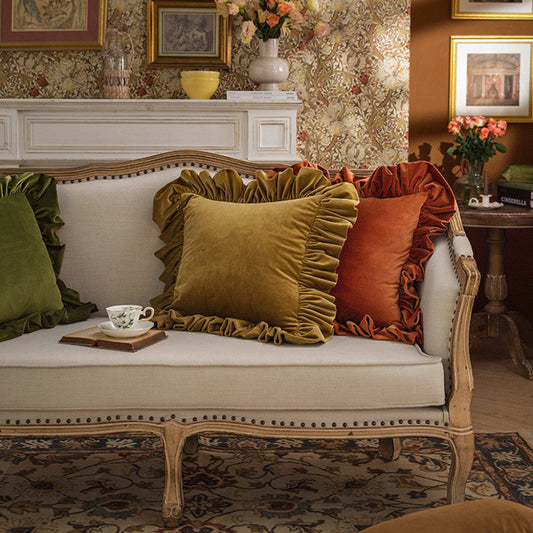 Decorative living room with a sofa featuring green and orange pillows, floral arrangements, and framed pictures.