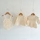 Three pieces of baby clothing on hangers against a white background