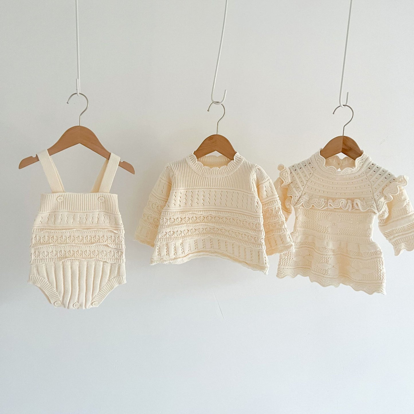 Three pieces of baby clothing on hangers against a white background