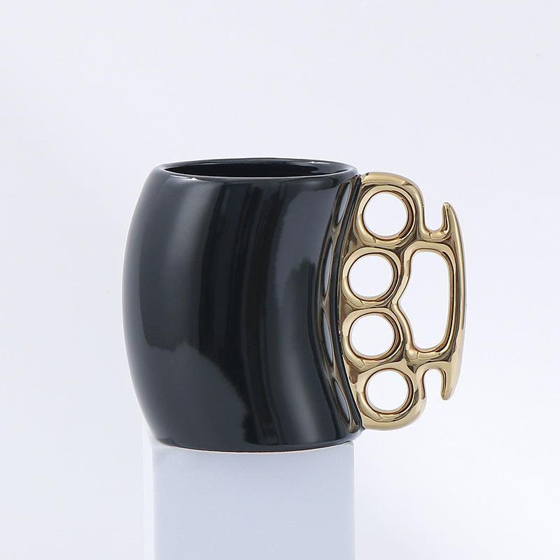 Black mug with a gold knuckle duster handle on a light gray background