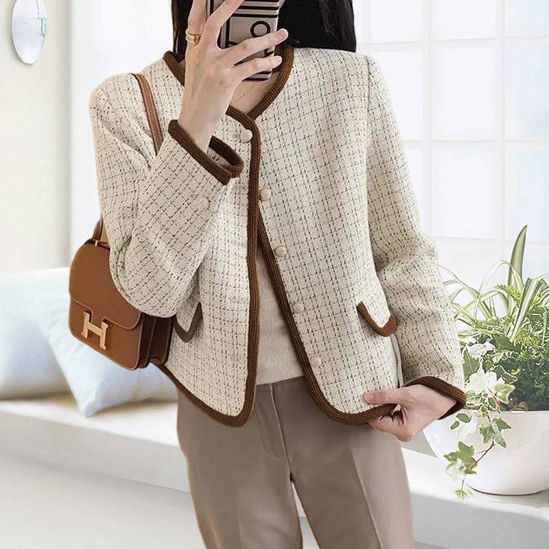 Person wearing a beige tweed jacket with brown trim, holding a brown handbag.