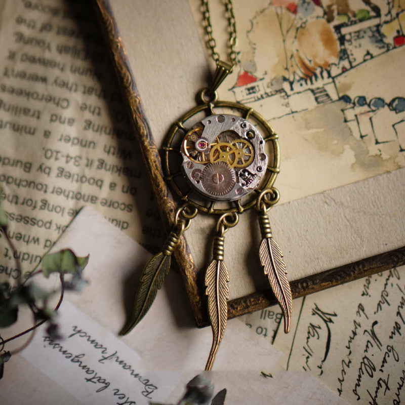 Vintage-style necklace with mechanical heart pendant and feathers on an old book background