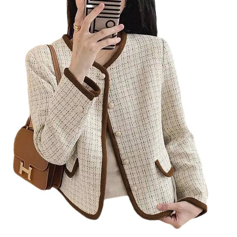 Beige tweed jacket with brown trim held by a person, with a brown handbag on a white background.