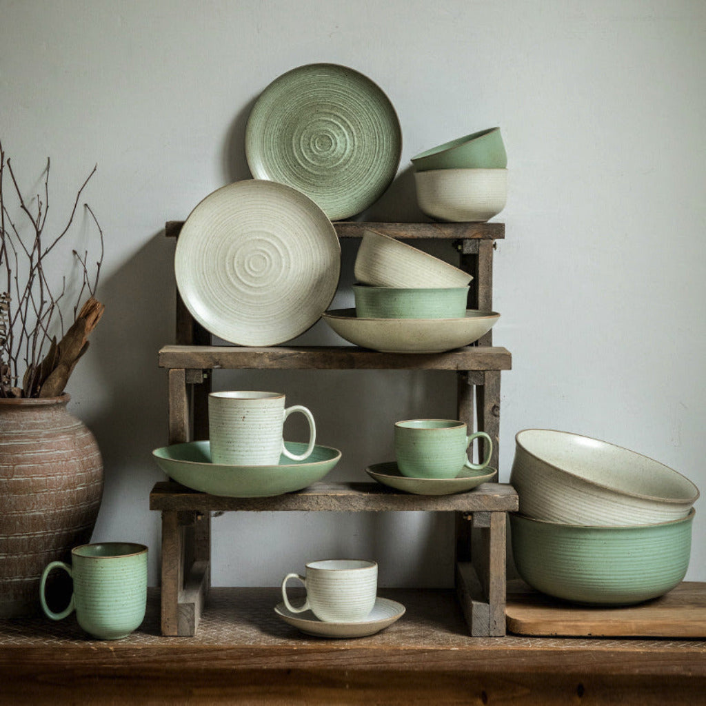 Collection of green ceramic dishes on wooden shelves against a neutral wall.