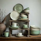 Collection of green ceramic dishes on wooden shelves against a neutral wall.