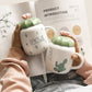 Two cactus-themed mugs held by hands with a product introduction sheet in the background.