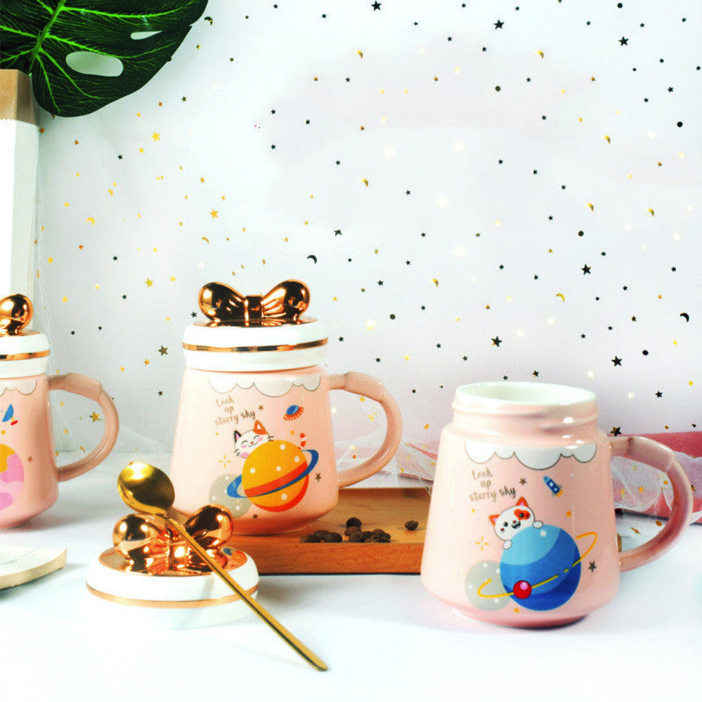Pink mugs with space-themed designs on a white surface with a starry background
