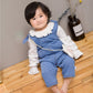 Child wearing a blue denim dress over a white shirt on a wooden floor.