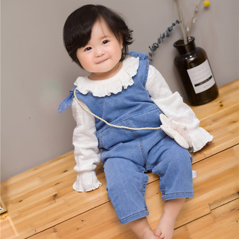 Child wearing a blue denim dress over a white shirt on a wooden floor.