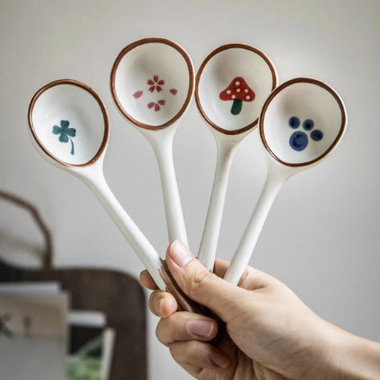 Five ceramic spoons with decorative ends held by a hand against a neutral background