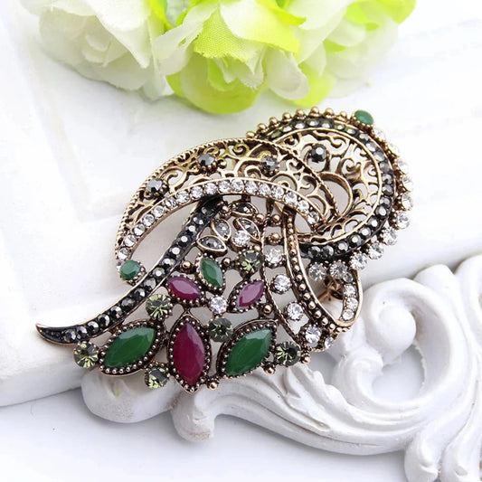 Decorative brooch with gemstones on a white surface with flowers in the background