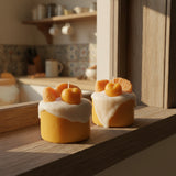 Two decorative candles shaped like pumpkins with white frosting on a reflective surface.