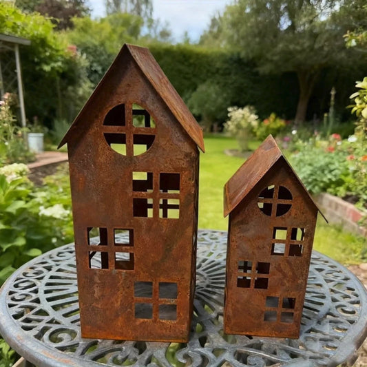 Two rust-colored house-shaped lanterns on a garden table with greenery in the background