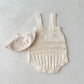 Knitted baby romper with lace details and matching hat on a light gray background