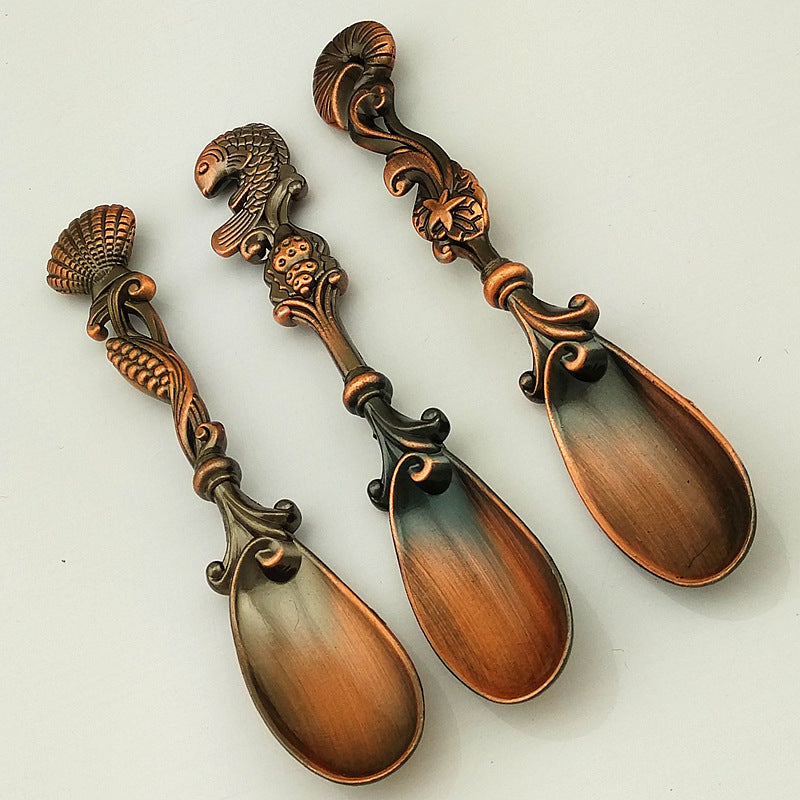 Three ornate copper spoons with decorative handles on a white background