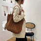Person holding a brown textured tote bag in an indoor setting