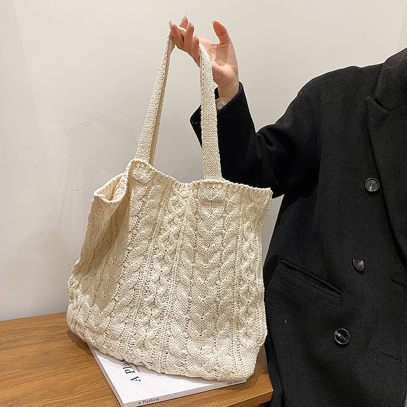 Person holding a textured beige tote bag on a wooden surface with a plain background