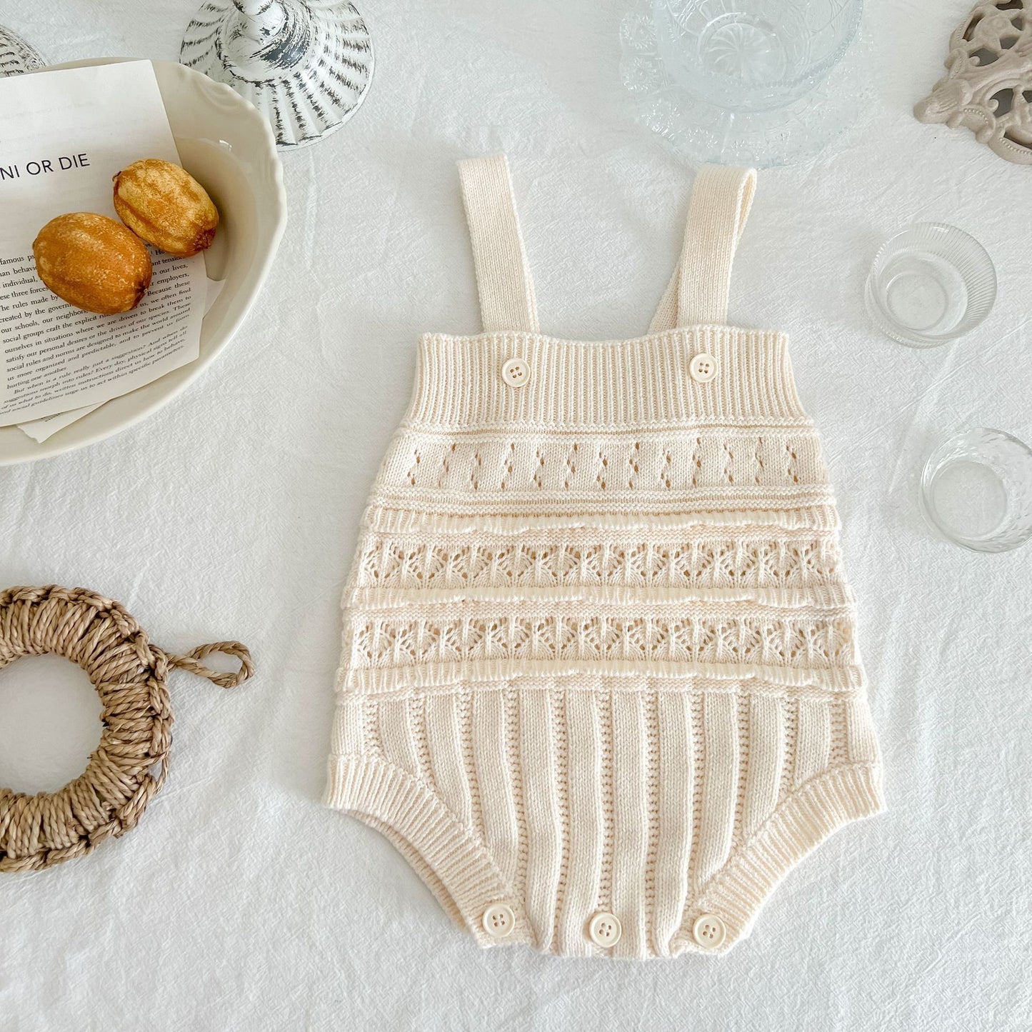 Beige knitted baby romper on a light surface with decorative items.