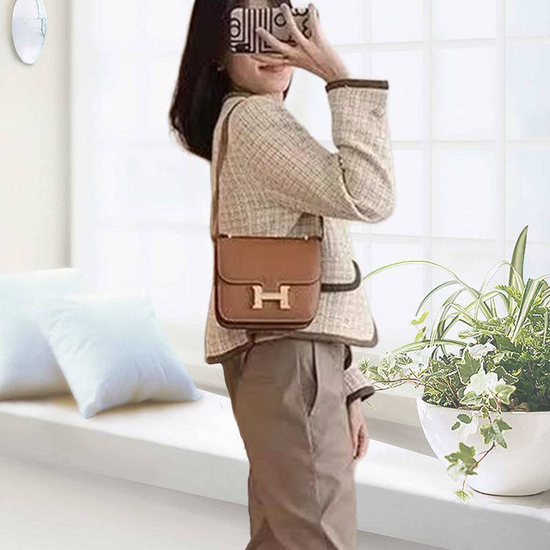 Person holding a brown handbag with a visible 'H' logo in a bright room.