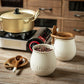 Ceramic sugar container with a wooden lid on a kitchen counter, next to a gold pot and coffee beans.