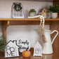 Decorative shelf with home decor items including a pitcher, pumpkins, and signs.