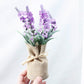 Bouquet of purple flowers wrapped in burlap with a bow on a light gray background
