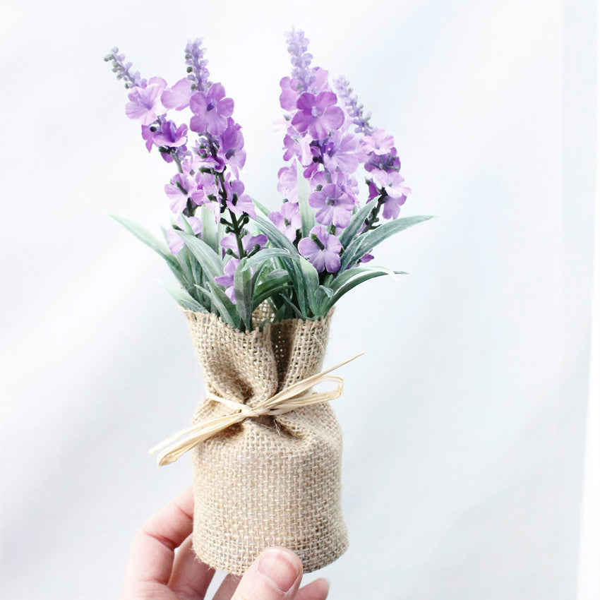 Bouquet of purple flowers wrapped in burlap with a bow on a light gray background
